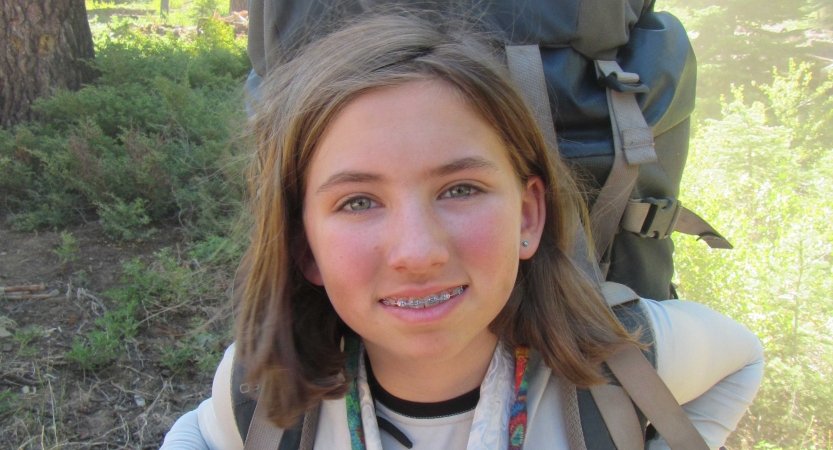 a young person wearing a backpack smiles at the camera